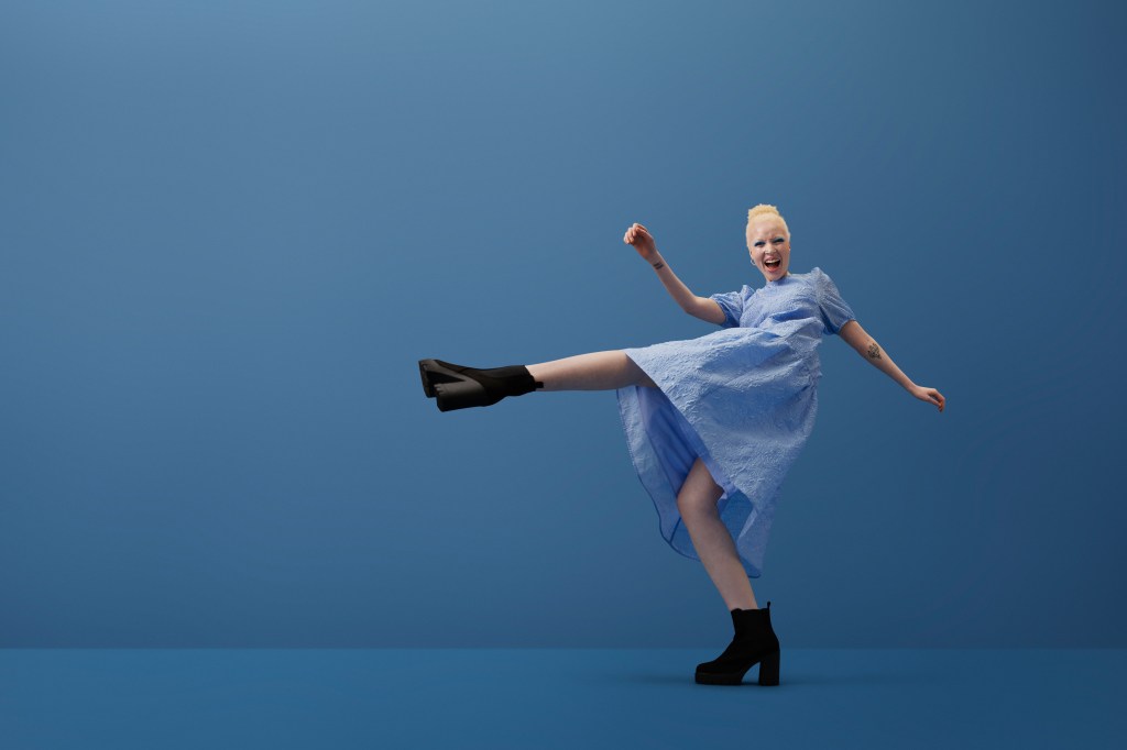 Full length portrait of albino young woman shouting while kicking leg against blue background