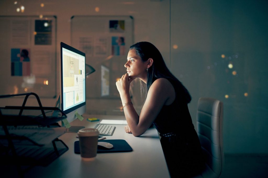 Shot of a young businesswoman using a computer at night in a modern office
